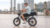 Rider on a HappyRun G70 electric delivery bike with a rear cargo bag along a city waterfront